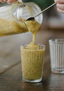 Crop unrecognizable person pouring tasty banana smoothie into glass placed on wooden table